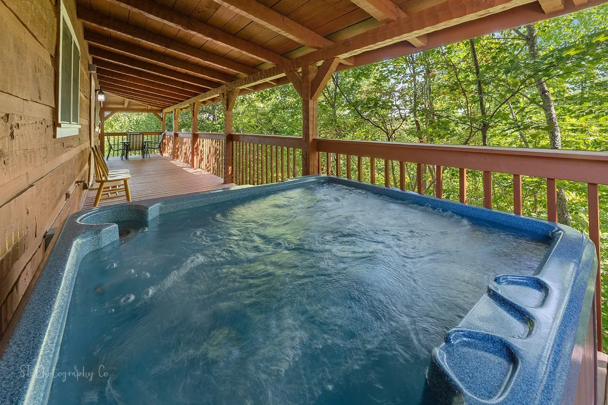 A tranquil exterior deck scene with a hot tub overlooking surrounding trees and wooden railing, ideal for relaxing and unwinding after a day of adventure.