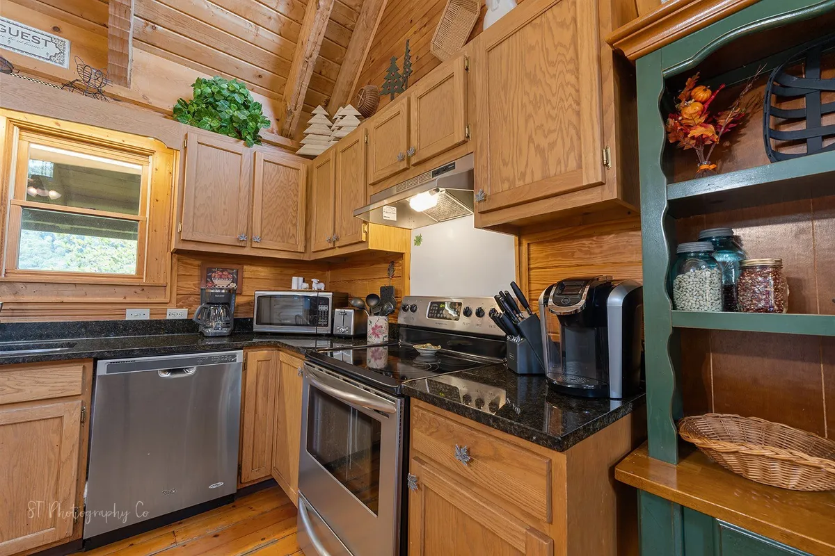 A warm, welcoming kitchen anchored by wooden cabinetry, gleaming stainless steel appliances, and a sleek black countertop. Decorative items on open shelves add character. The space is designed for cooking, entertaining, and group gatherings, with plenty of counter space and modern amenities.