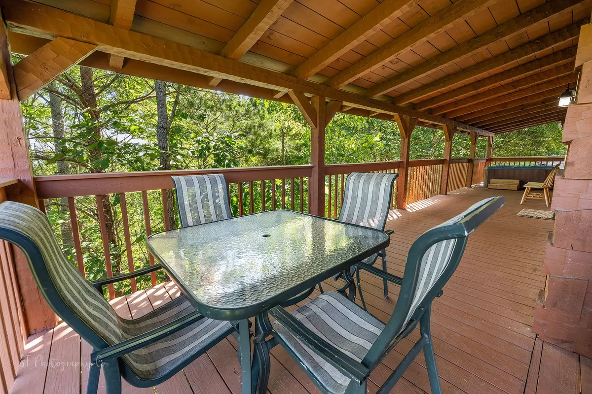 An inviting outdoor dining space with a glass table and striped chairs, surrounded by trees and set against a wooden railing. The area is ideal for shared meals, sunset cocktails, or morning coffee together while soaking in the scenery.