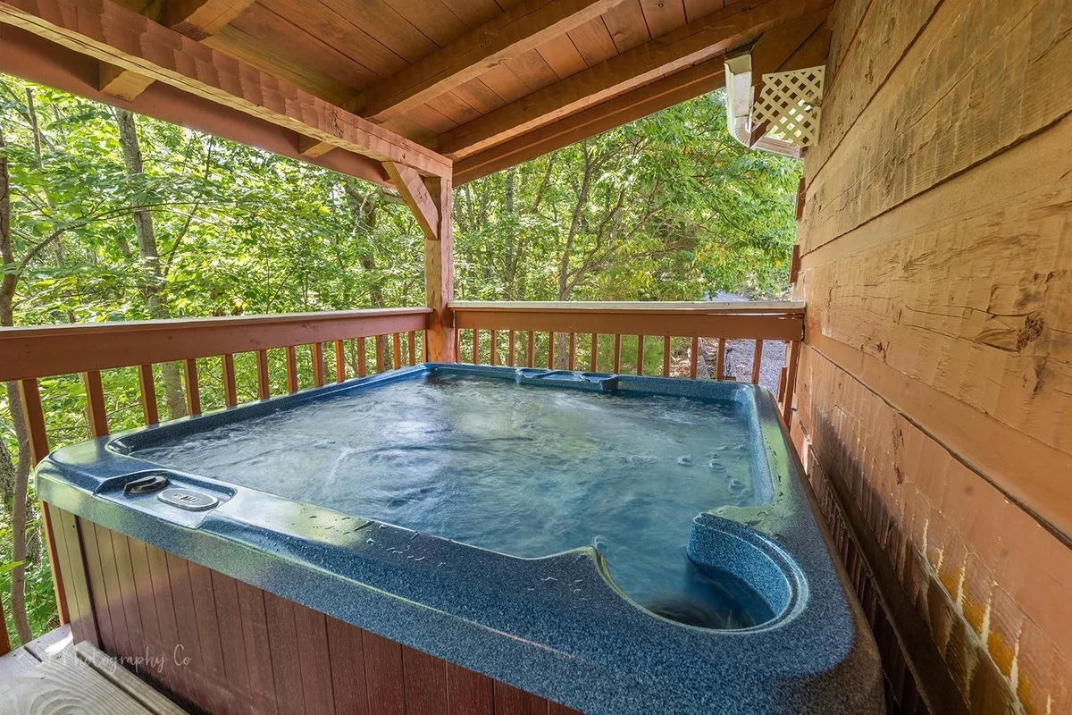 This exterior image features a private hot tub situated on a wooden deck surrounded by lush foliage. The scene exudes tranquility, with the hot tub inviting guests to unwind while enjoying the sunset or starlit nights over the treetops.