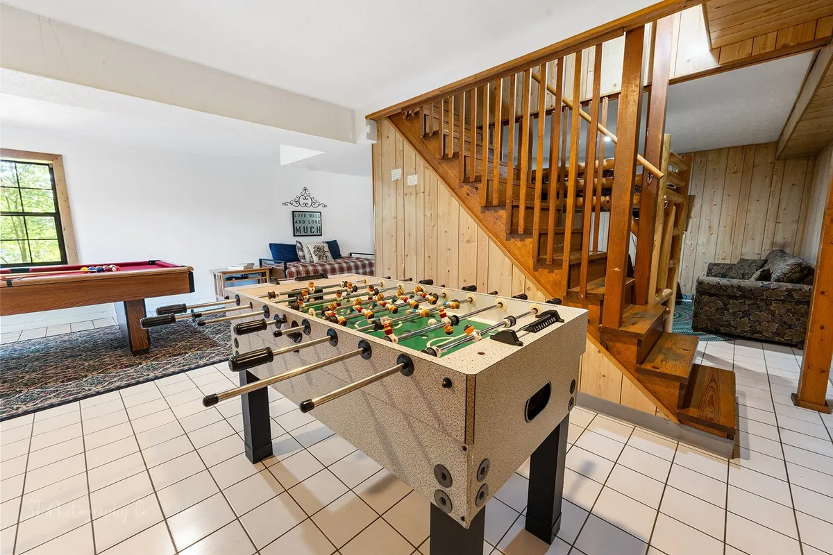 A vibrant interior scene featuring both a foosball table and a pool table, with a staircase and comfortable seating nearby. The space is clearly designed for fun, games, and lively group interactions.