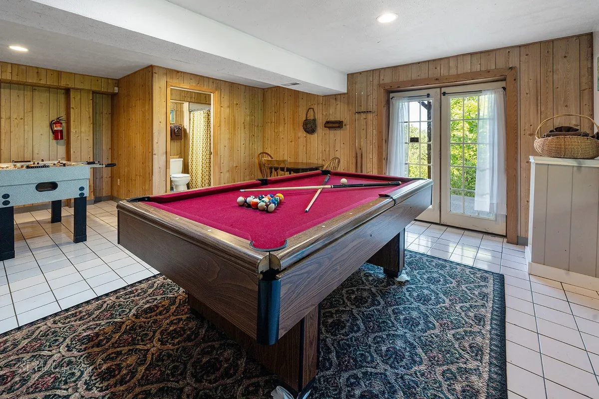 A dynamic interior shot capturing both a pool table and a foosball table, set in a warm, wood-accented environment with French doors providing natural light and a welcoming atmosphere for friendly tournaments.