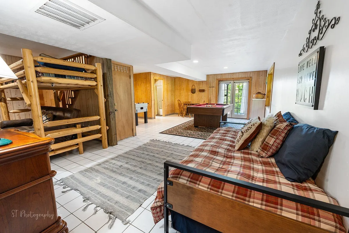A welcoming nook with bunk beds, a game table, plaid bedding, and charming wooden accents, creating an ideal hangout space for family game nights, reading, or casual relaxation.