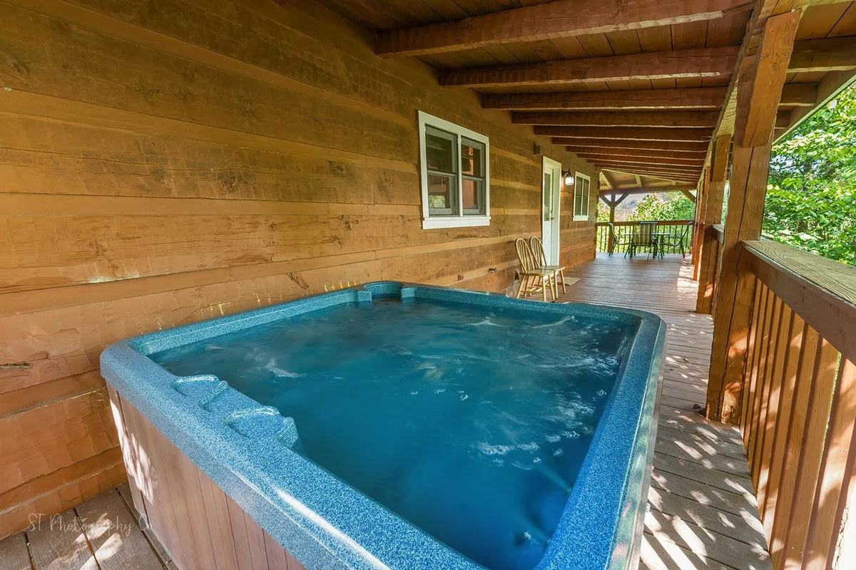 A hot tub set on a wooden deck, surrounded by lush greenery, featuring enough space for a group to relax and unwind together. The ambiance is tranquil, reflecting the soothing aspect of the retreat experience.